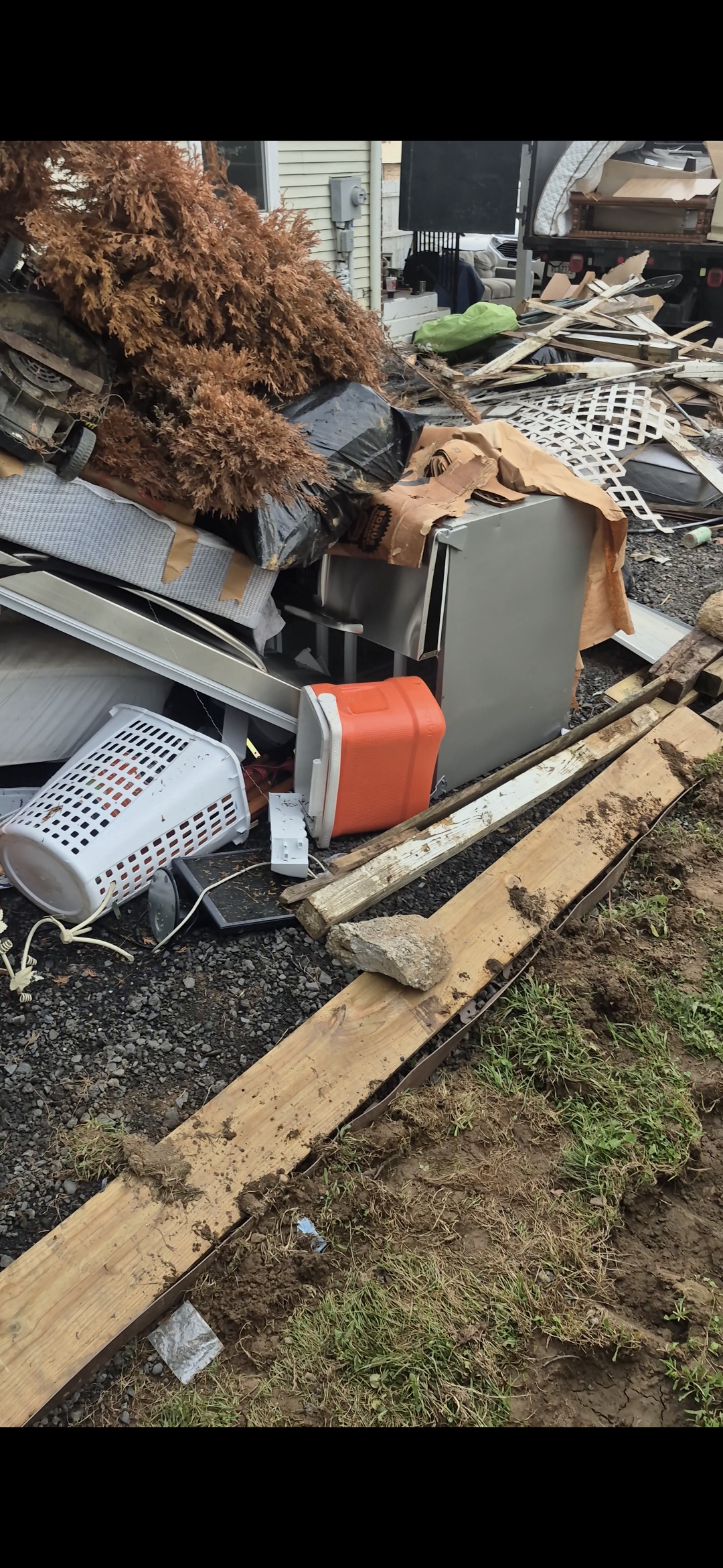 Curbside junk pile with a lawn mower, laundry baskets, a cooler, and lumber being loaded into an HS Hauling dump truck