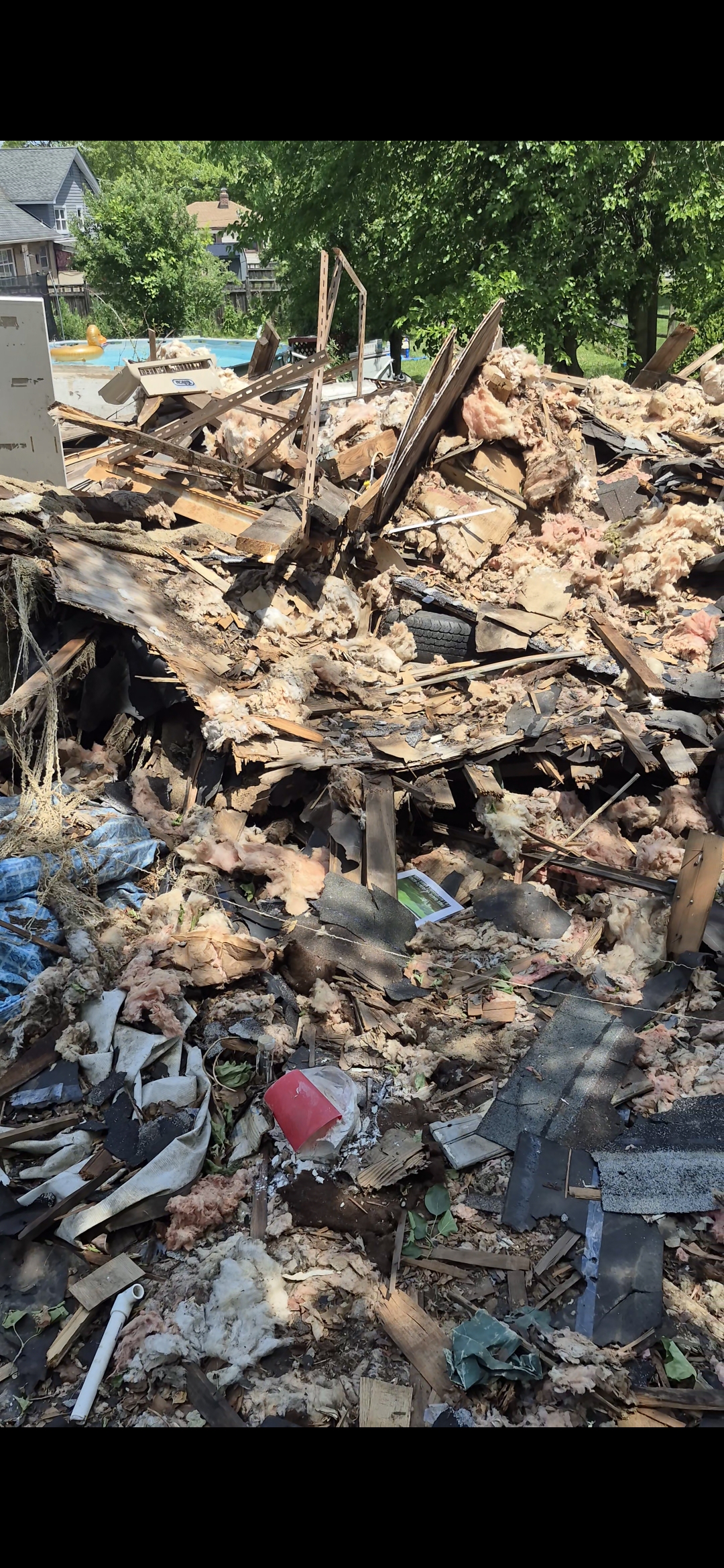 Massive pile of demolished building debris including lumber, insulation, and shingles awaiting removal